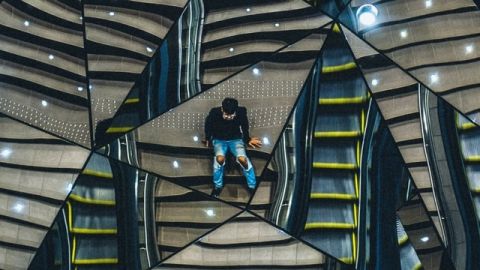 un homme assis sur des escaliers, se reflétant dans plusieurs miroirs