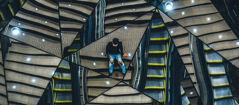 miroir un homme assis sur des escaliers, se reflétant dans plusieurs miroirs