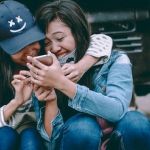 deux amies rient ensemble devant leur smartphone