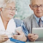 Deux seniors, un homme et une femme, en train de tenir une carte bancaire, un téléphone et une tablette