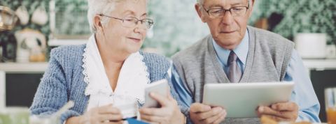 Seniors Deux seniors, un homme et une femme, en train de tenir une carte bancaire, un téléphone et une tablette