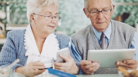Deux seniors, un homme et une femme, en train de tenir une carte bancaire, un téléphone et une tablette