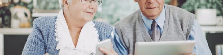 Deux seniors, un homme et une femme, en train de tenir une carte bancaire, un téléphone et une tablette