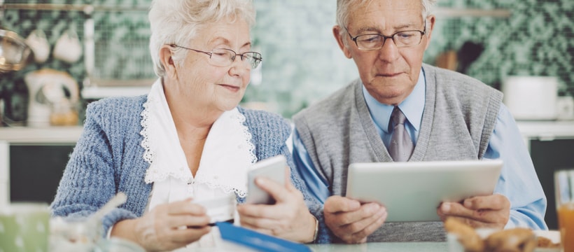 Seniors Deux seniors, un homme et une femme, en train de tenir une carte bancaire, un téléphone et une tablette