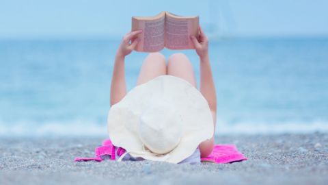 Une femme allongée sur la plage en train de lire un livre