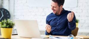 Un jeune homme en train de se réjouir derrière son ordinateur portable