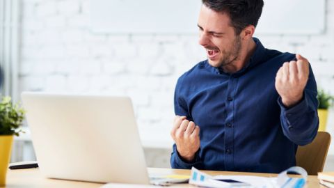 Un jeune homme en train de se réjouir derrière son ordinateur portable