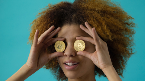 Une femme tient deux bitcoins au niveaux de ses yeux