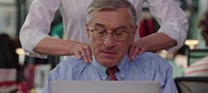 Robert de Niro, dans le film Le Stagiaire, en train de travailler à son bureau et de se faire masser