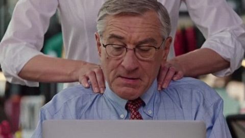 Robert de Niro, dans le film Le Stagiaire, en train de travailler à son bureau et de se faire masser