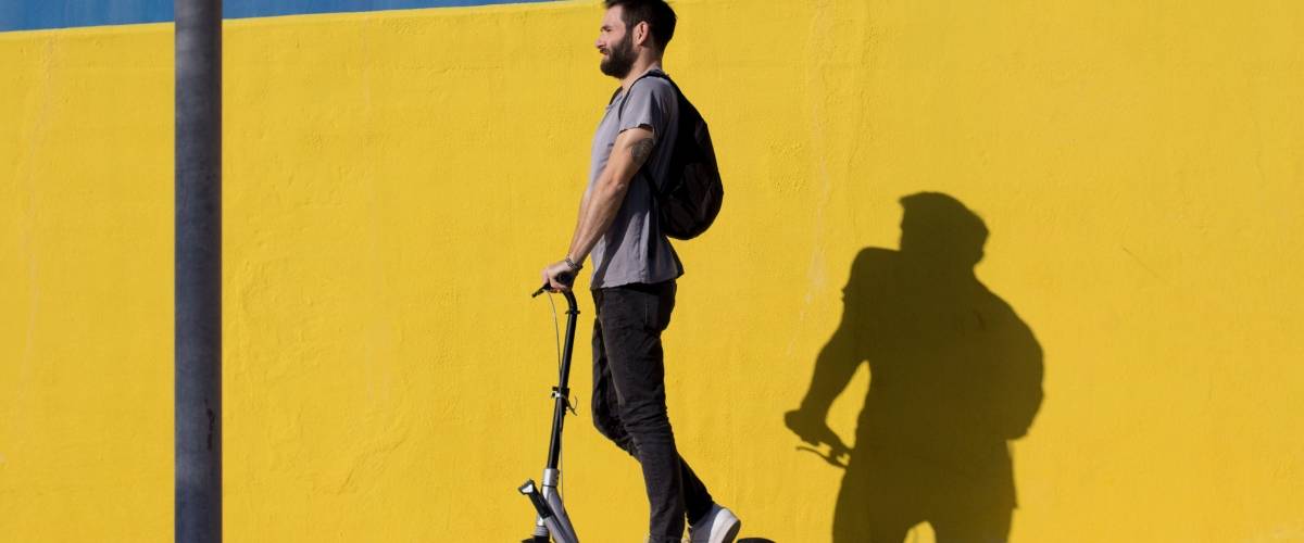 Les trottinettes en libre service envahissent la ville Un homme sur une trottinette devant un mur jaune