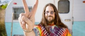 Un hippie devant une caravane en train de faire le signe peace