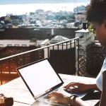 une femme noire tape sur son ordinateur sur un balcon