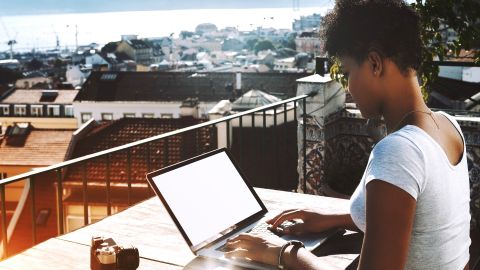 une femme noire tape sur son ordinateur sur un balcon