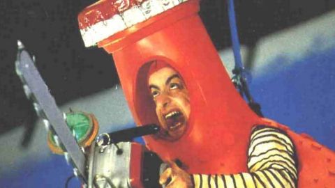 un homme dans un costume orangina rouge tient une tronçonneuse