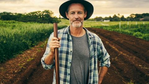 Un agriculteur portant un chapeau et une chemise à carreau, tenant une fourche, dans un champ
