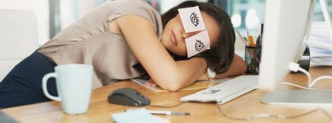 Comment respecter le droit à la déconnexion en entreprise ? Une femme en train de dormir sur son bureau devant son ordinateur avec des post-it sur les yeux