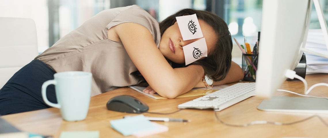 Comment respecter le droit à la déconnexion en entreprise ? Une femme en train de dormir sur son bureau devant son ordinateur avec des post-it sur les yeux