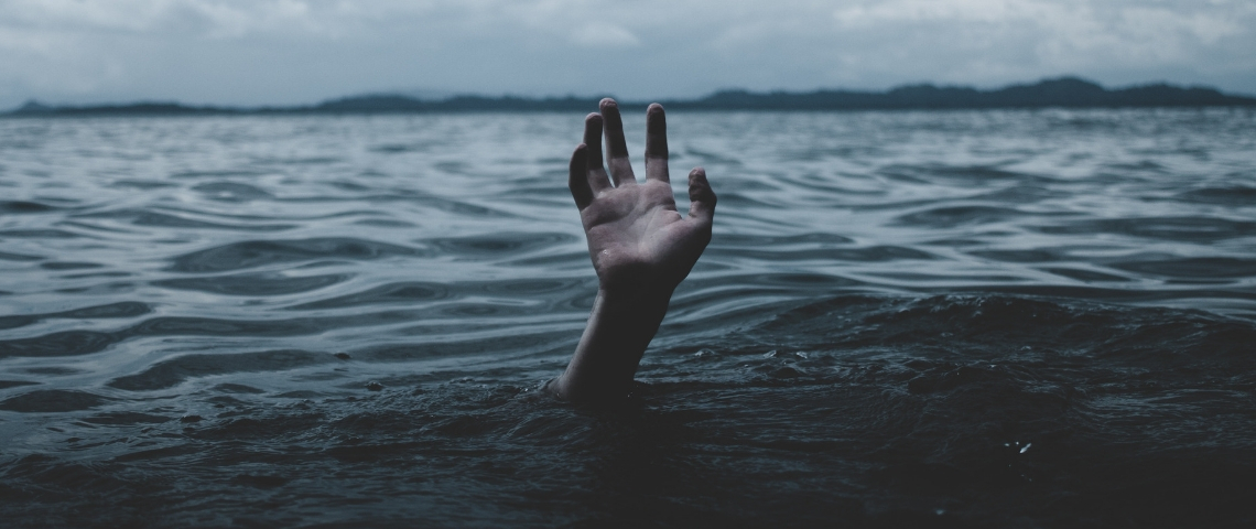 une main essaie de sortir de l'eau, un homme se noie
