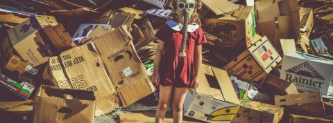 Faut-il faire les soldes ? Une petite fille avec un masque à gaz devant un amoncellement de cartons