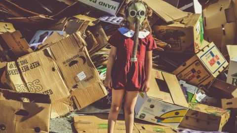 Une petite fille avec un masque à gaz devant un amoncellement de cartons