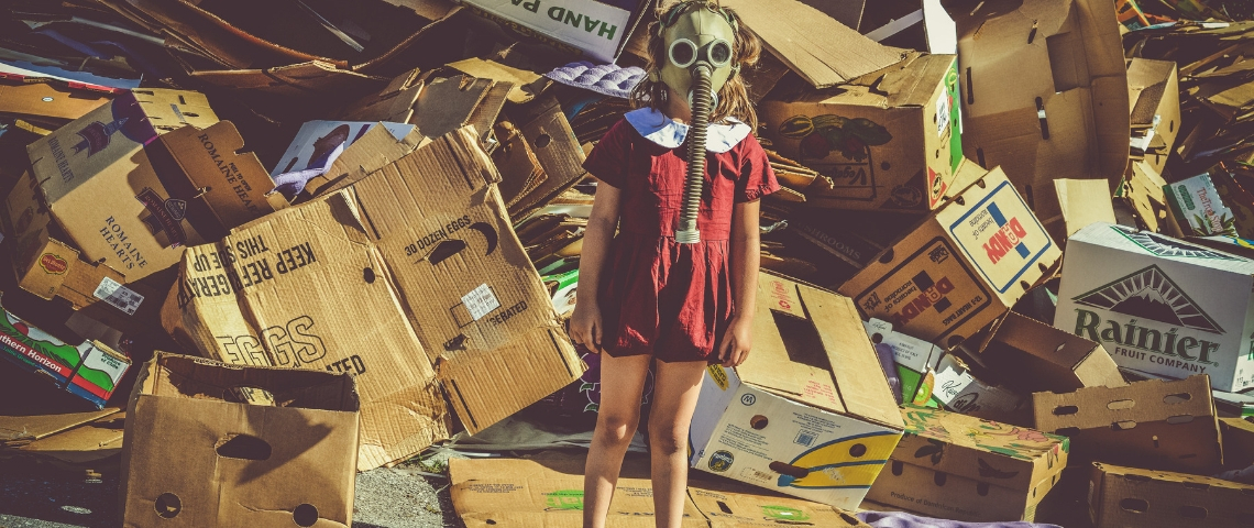 Faut-il faire les soldes ? Une petite fille avec un masque à gaz devant un amoncellement de cartons
