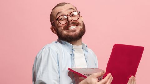 un homme souriant travaille sur son ordinateur rouge