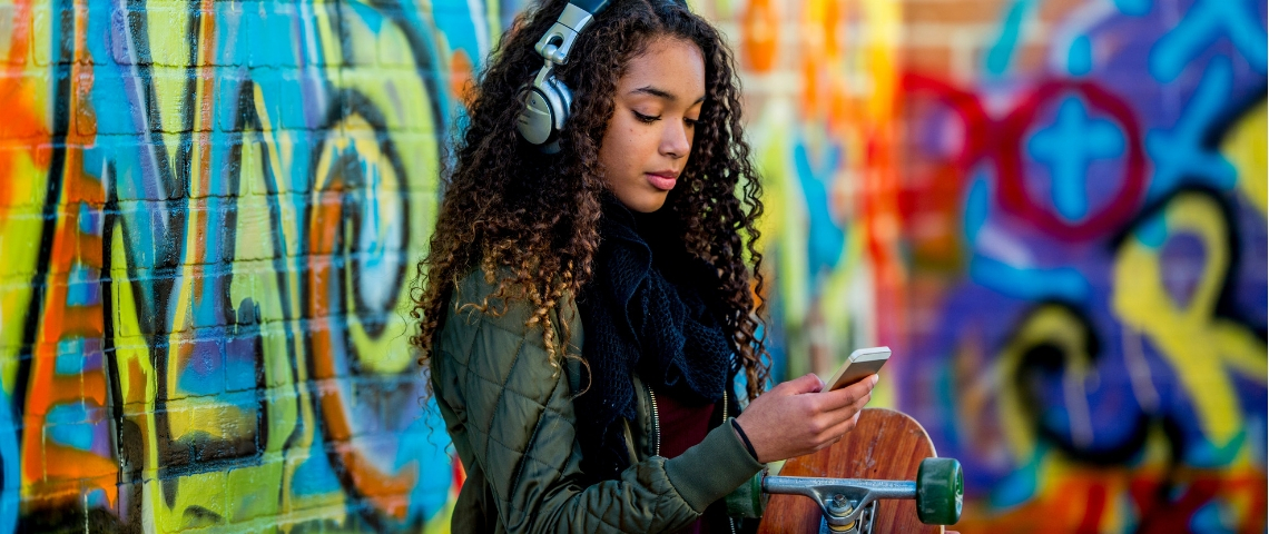 Savez-vous parler aux Zillennials ? Une adolescente avec un casque sur les oreilles qui regarde son téléphone