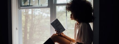 Une femme noire lit à côté de sa fenêtre