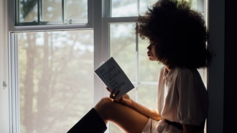 Une femme noire lit à côté de sa fenêtre