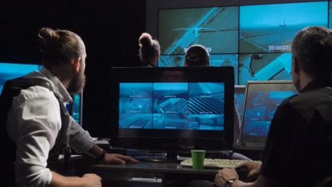 Des hommes dans une piece sombre qui regardent des écrans