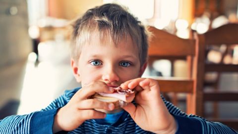 un jeune garçon mange un sandwich au jambon