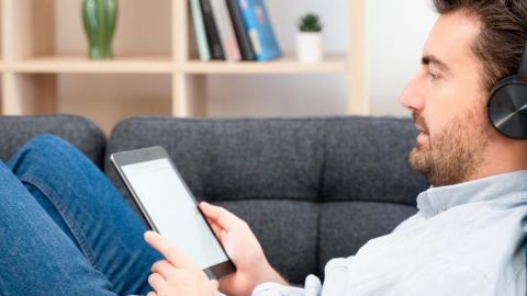 homme allongé dans un canapé avec un casque et une liseuse