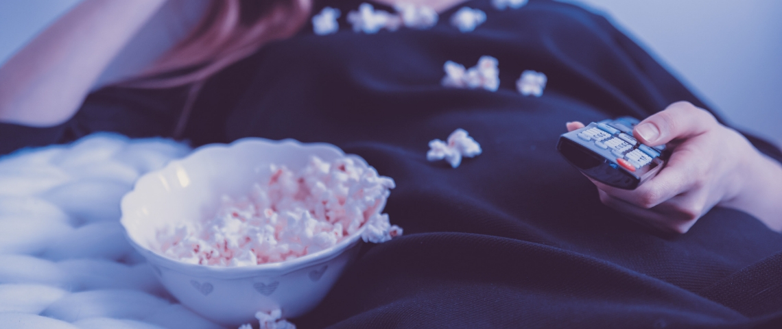 Apprendre une langue en regardant Netflix Une femme qui regarde la télé en mangeant du popcorn