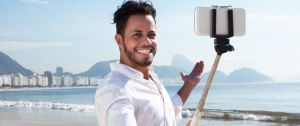 Jeune homme à la plage, se prenant en photo avec une perche à Selfie