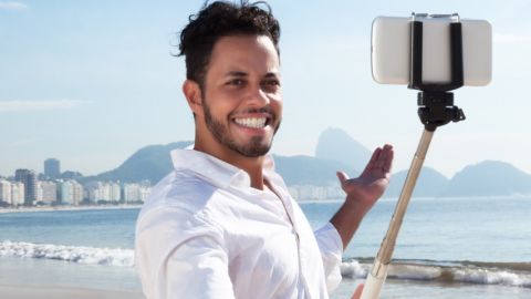 Jeune homme à la plage, se prenant en photo avec une perche à Selfie