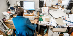 Un homme de dos, assis à son bureau mal rangé