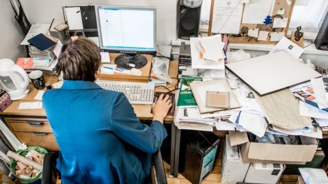 Un homme de dos, assis à son bureau mal rangé