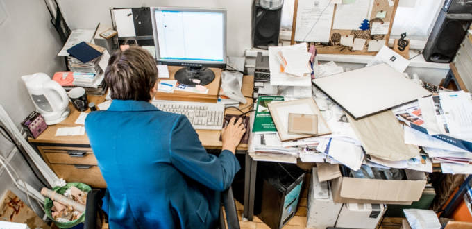 Un homme de dos, assis à son bureau mal rangé