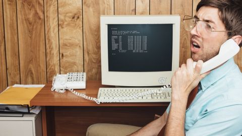 Un homme interloqué au téléphone, derrière un ordinateur rétro