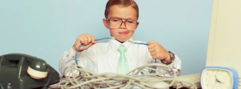 Pour gérer ses données, mieux vaut bien s'équiper Un enfant habillé en tenue de travail dans un bureau en train d'essayer de brancher deux câbles