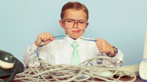 Un enfant habillé en tenue de travail dans un bureau en train d'essayer de brancher deux câbles