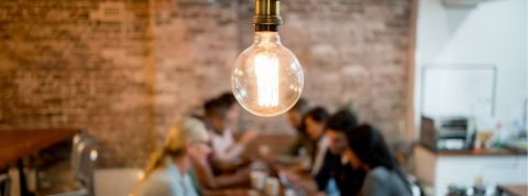 Une ampoule sur fond flouté de personnes qui travaillent sur un bureau