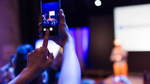 Une personne en train de photographier une prise de parole scénique avec son téléphone portable
