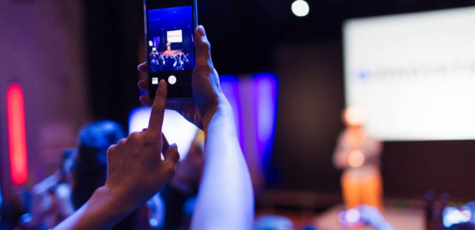 Une personne en train de photographier une prise de parole scénique avec son téléphone portable