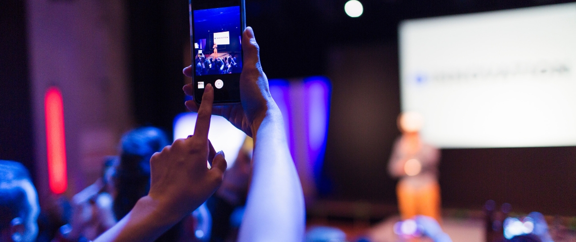 Quelles tendances pour l'événementiel 2019 ? Une personne en train de photographier une prise de parole scénique avec son téléphone portable