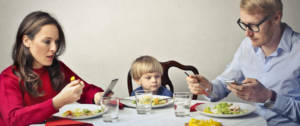 Un homme et une femme à table en train de regarder leur smartphone pendant qu'un enfant est seul au milieu