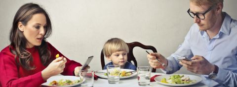 Internet et les écrans ont-ils tué la vie de famille ? Un homme et une femme à table en train de regarder leur smartphone pendant qu'un enfant est seul au milieu