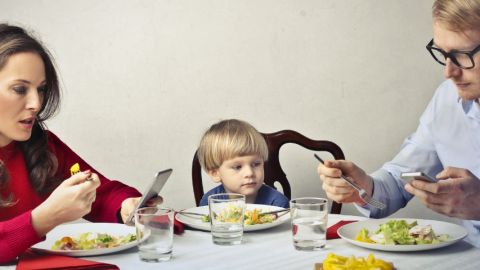Un homme et une femme à table en train de regarder leur smartphone pendant qu'un enfant est seul au milieu