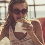 Une femme à la plage qui prend un selfie en mangeant un burger